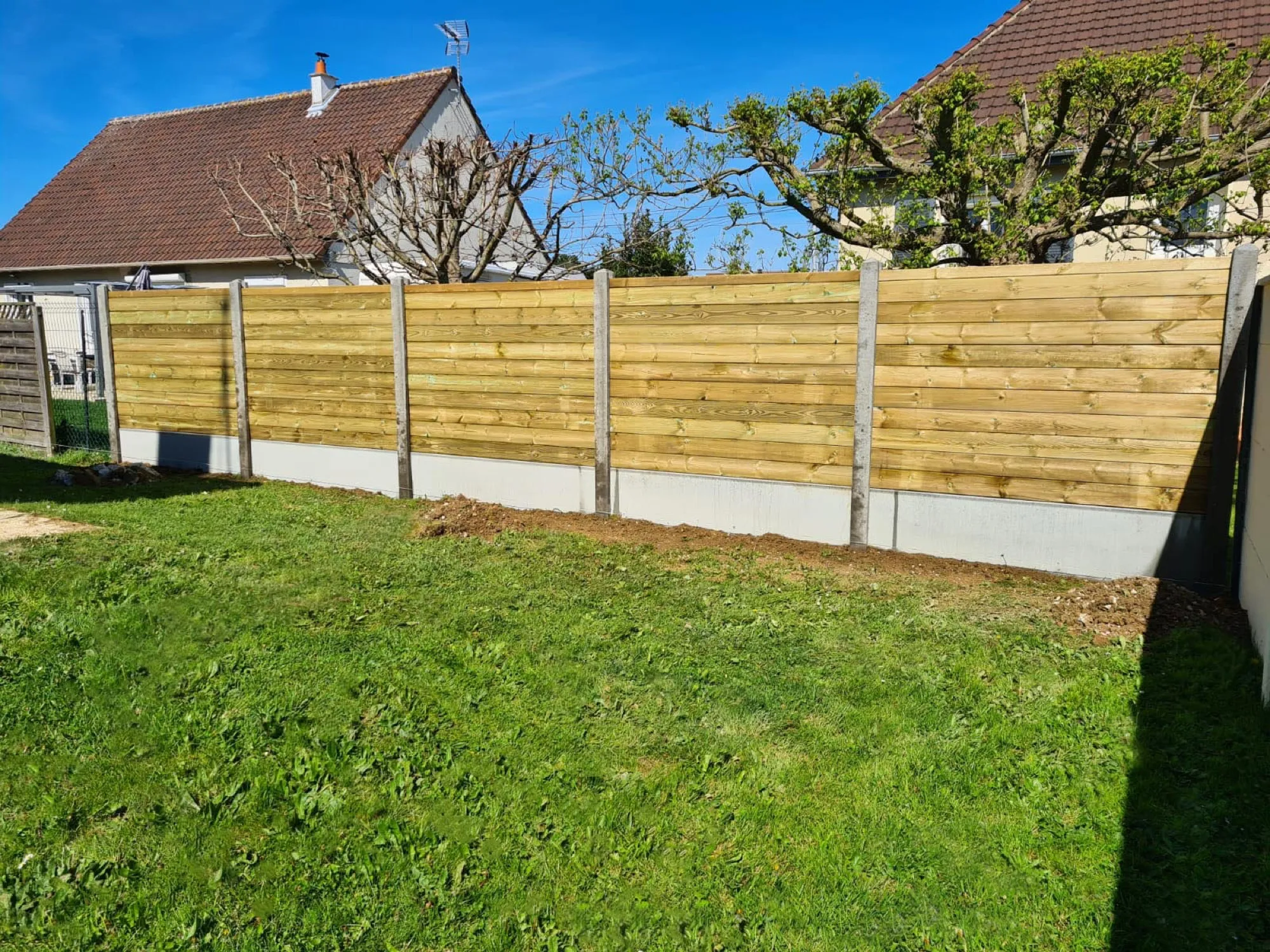 Clôture en lames de bois sur soubassement béton en limite de jardin