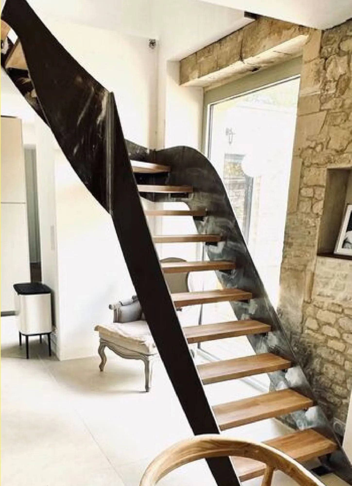 Escalier sur mesure à limon métallique cintré et marches en bois, devant un mur en pierre