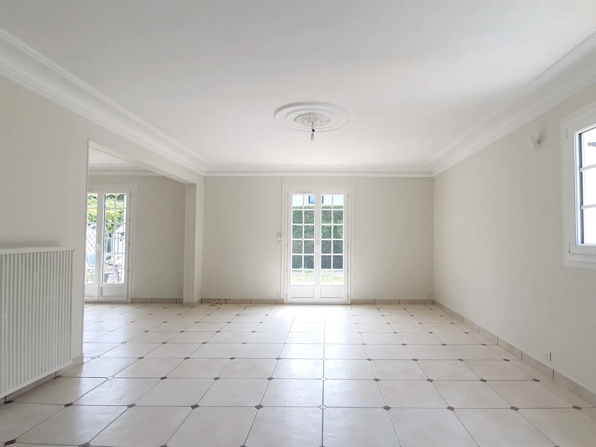 Grand séjour repeint en blanc, moulures au plafond et carrelage clair