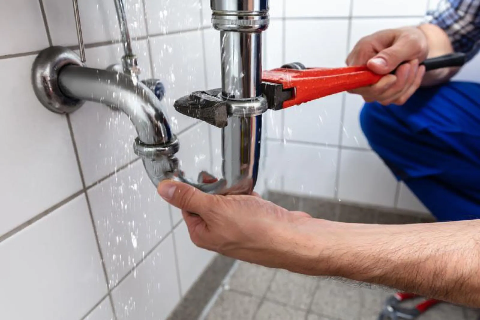 Plombier resserrant le siphon d’un lavabo à la clé à molette