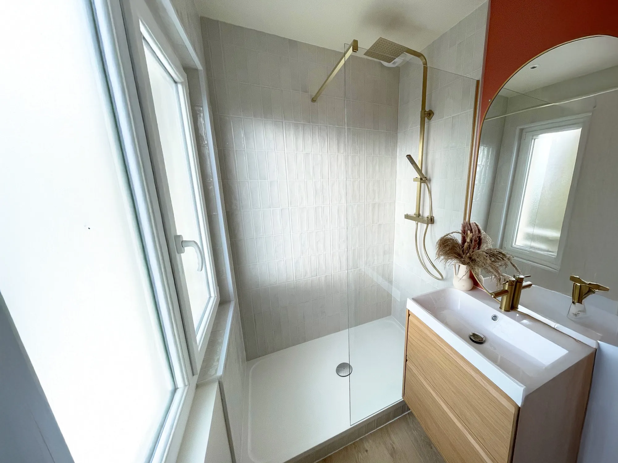 Salle de bain avec douche à l’italienne, robinetterie dorée et miroir arrondi