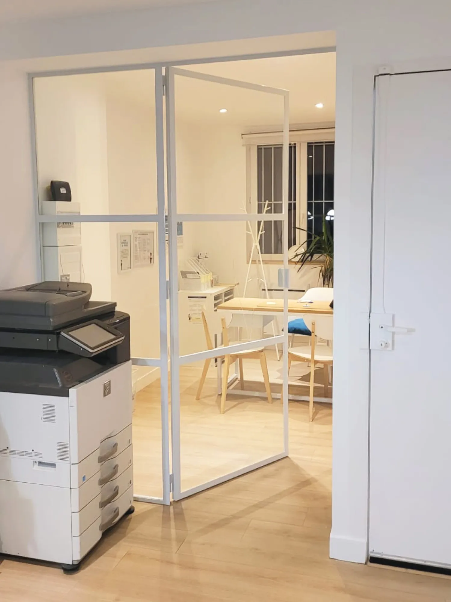 Verrière d’atelier blanche avec porte, séparant un bureau lumineux